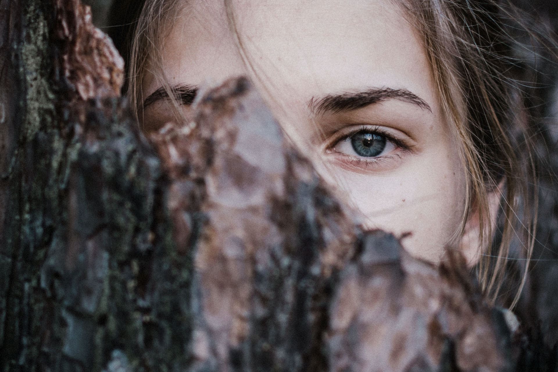 Gesicht einer Frau halb hinter Baumrinde versteckt