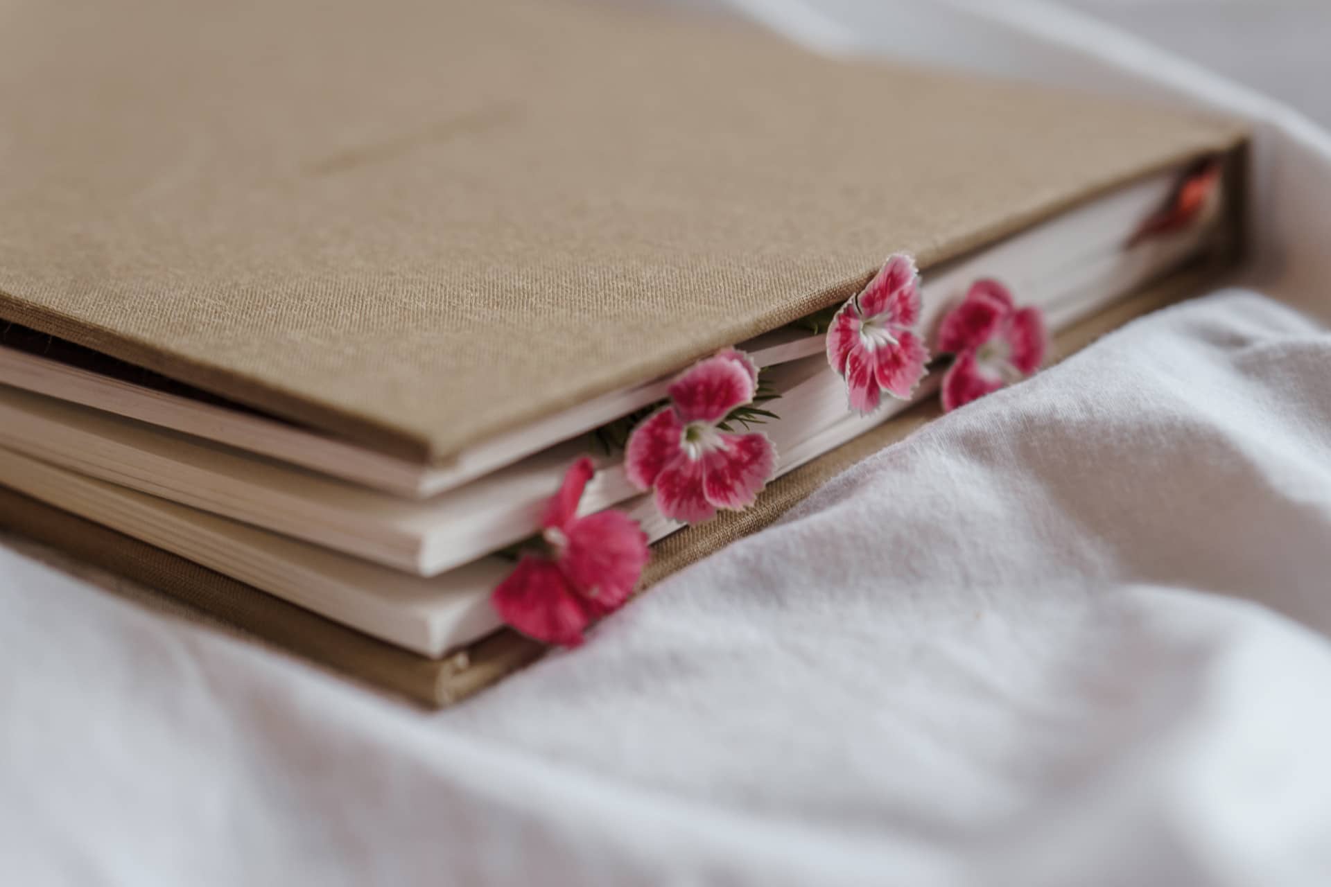 Geschlossenes Notizbuch mit braunem Leineneinband und vier pinken Blüten zwischen den Seiten