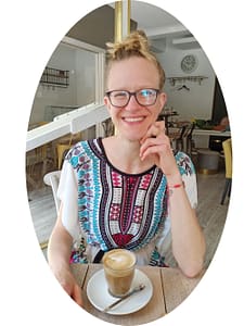 Lisa in bunter Tunika in einem Café, lächelnd, mit einem Flat White Kaffe vor ihr