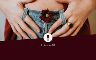 Photo of the belly of a white person with blue jeans on, a dark red flower in their buttonhole, hands leisurely on the belly and intertwined in the belt loop