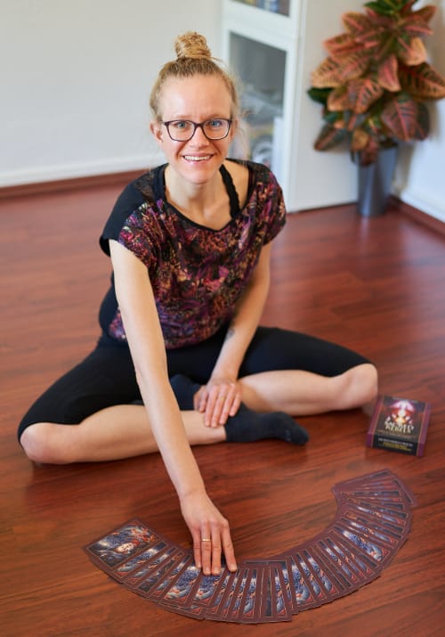 Lisa Jara sitting on the floor with the Sacred Rebels Oracle Deck spread out in front of her, looking into the camera