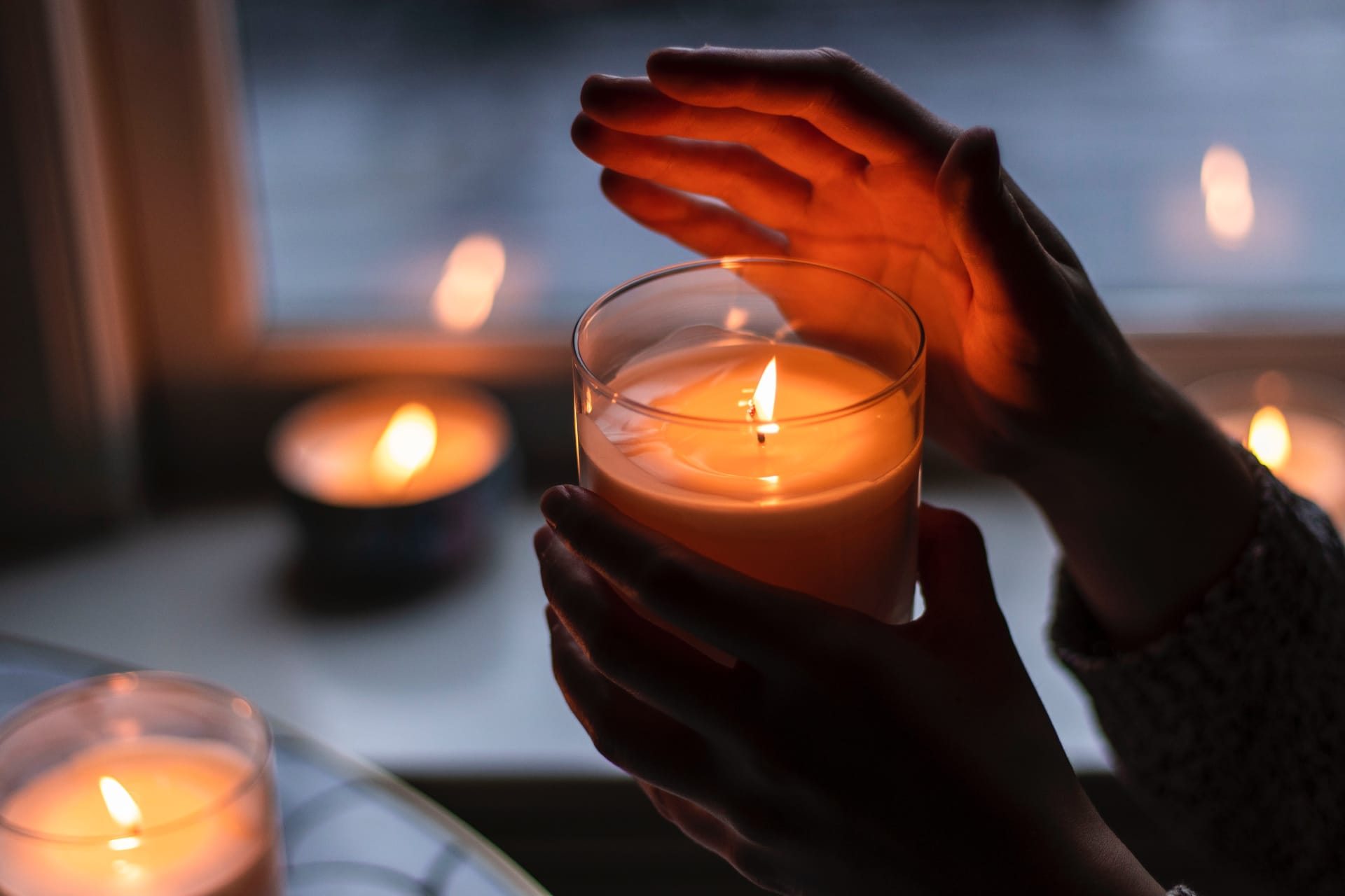 Eine Hand, die eine Kerze hält und weitere Kerzen im Hintergrund auf einem Fensterbrett